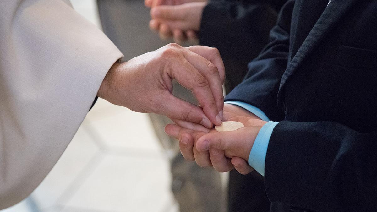 Priesterhand legt eine Hostie in die offenen Hände eines Kindes