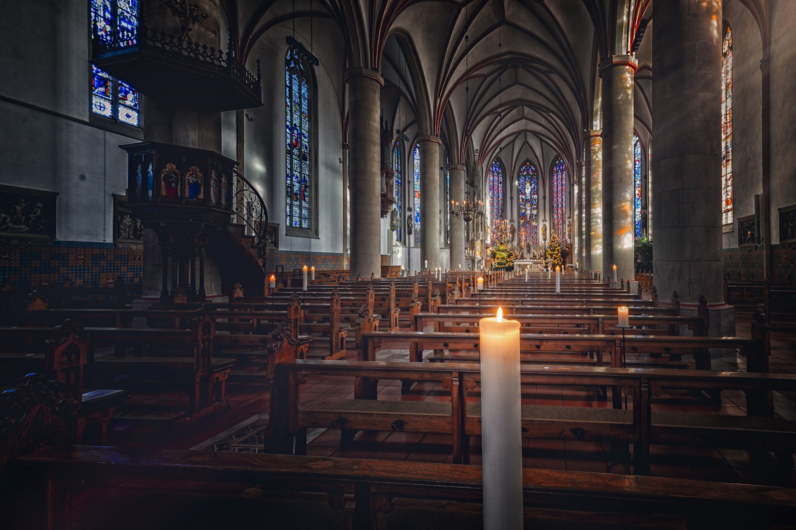 Brennende Kerze im Mittelgang einer gotischen Kirche